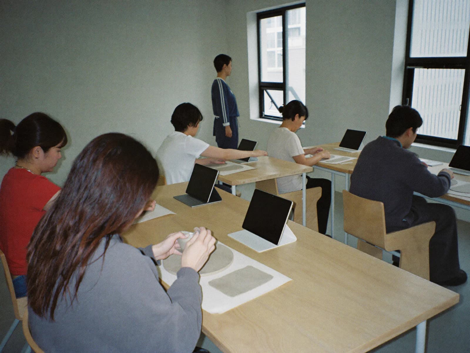 밝은 작업실의 일일 도자기 수업. 참가자마다 앞에 작은 태블릿을 세워 두고 흙을 빚고 있습니다.